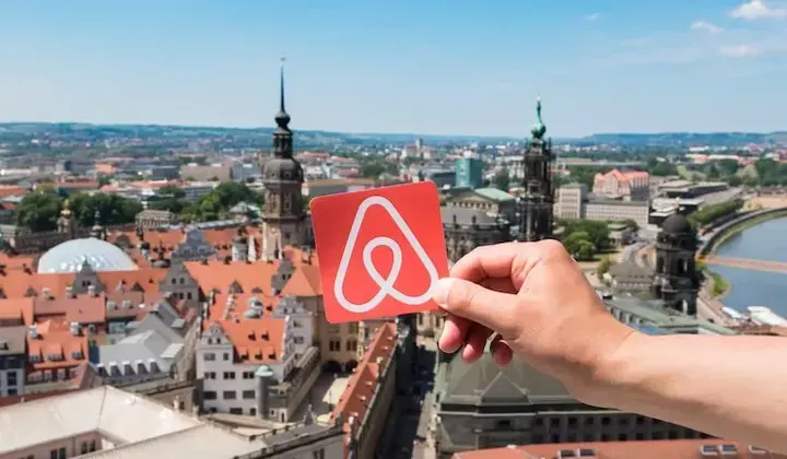 Mano sosteniendo una tarjeta con el logo de Airbnb sobre los techos de una ciudad