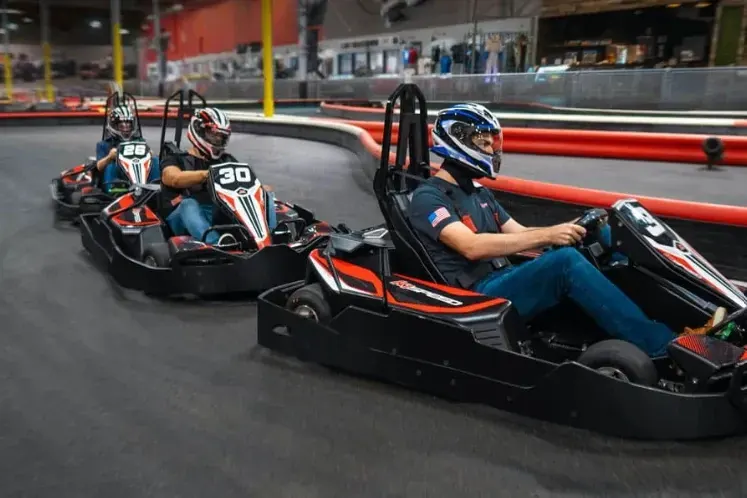 Pilotos con casco compitiendo en una pista de karts cubierta