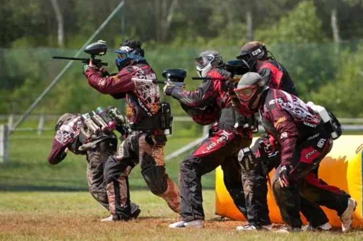 Jugadores de paintball con máscaras avanzando en un campo abierto