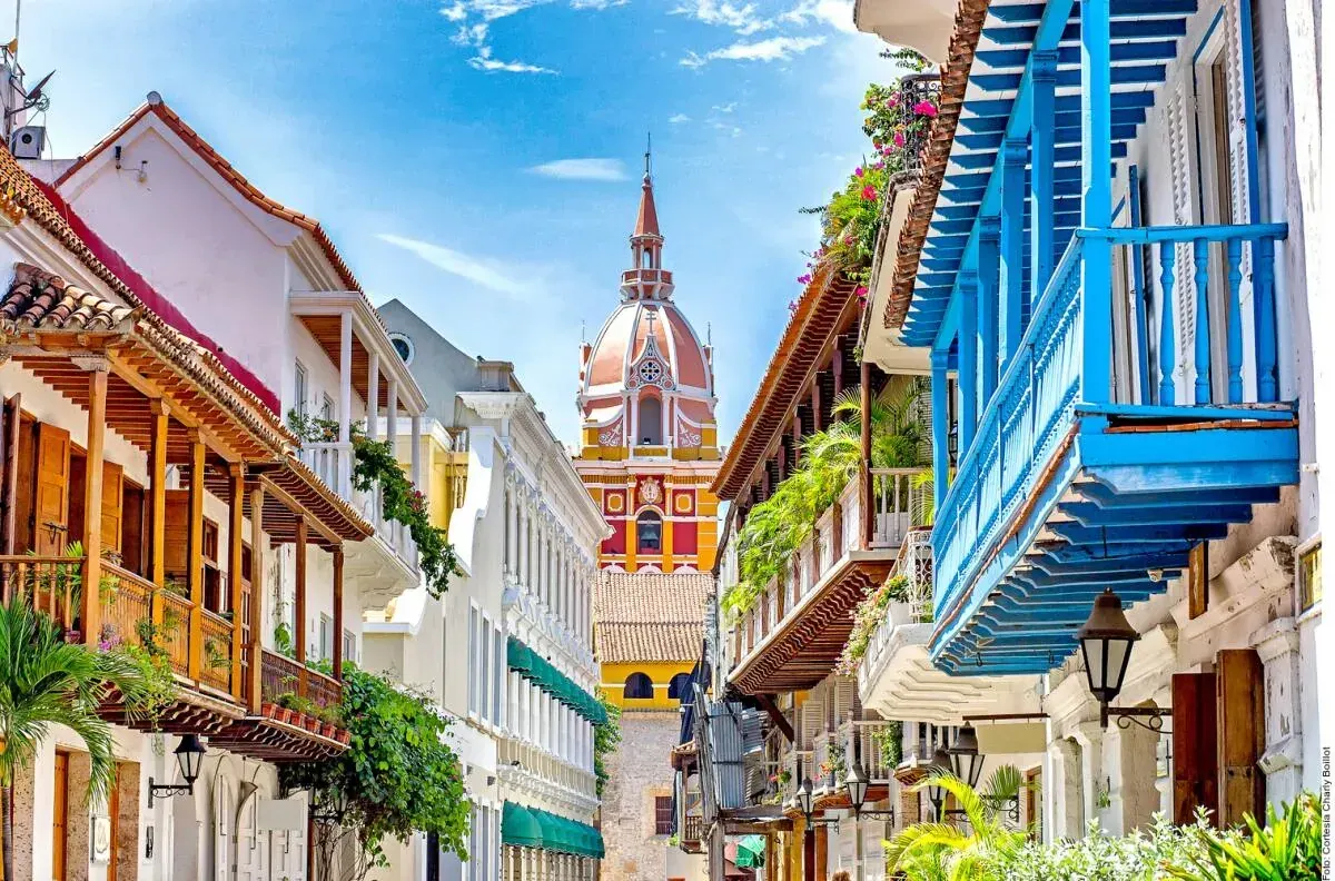 Calle colonial de Cartagena con balcones de madera de colores y la cúpula de una iglesia